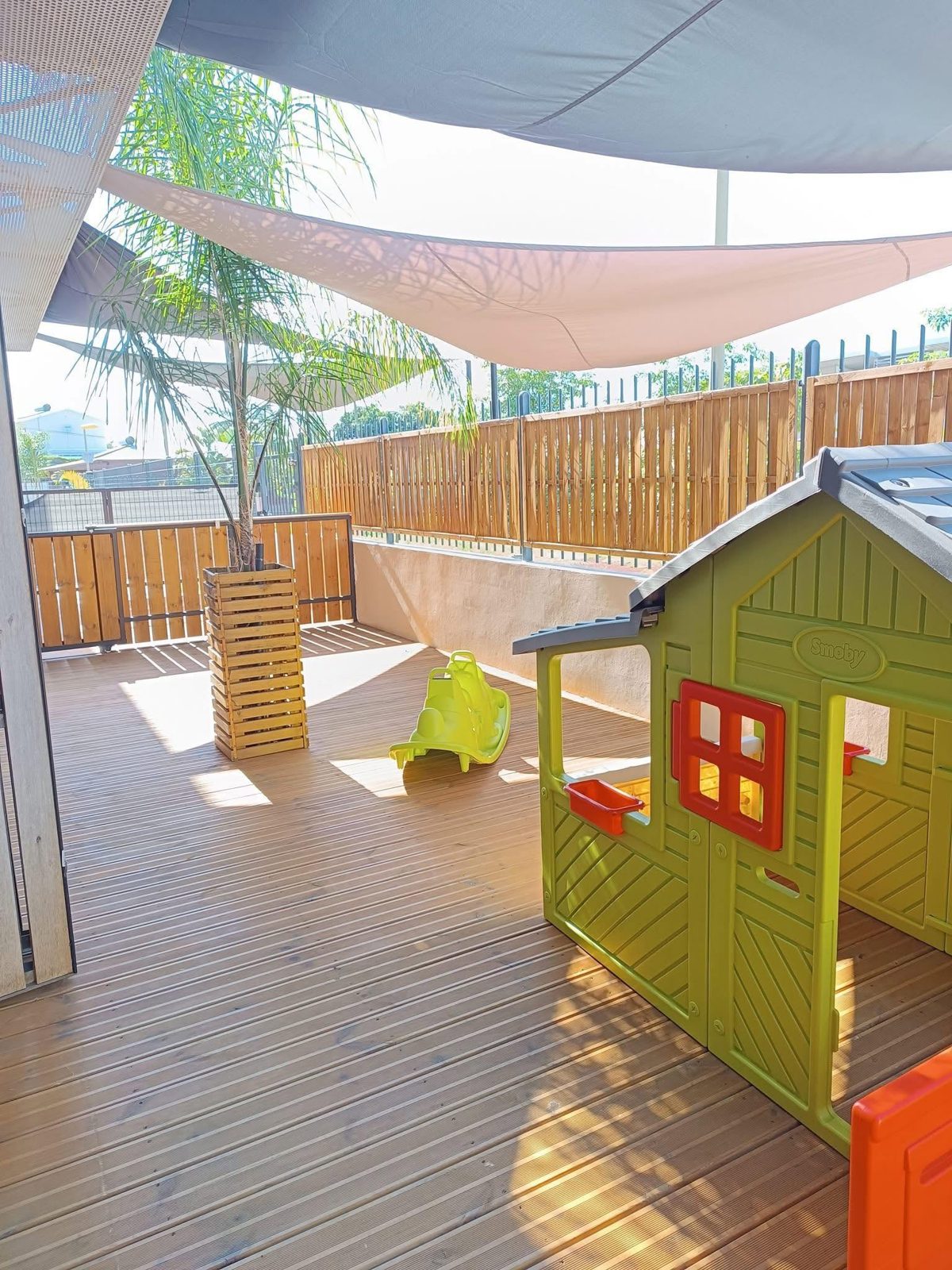Terrasse ombragée de la crèche avec sa maisonnette de jeu